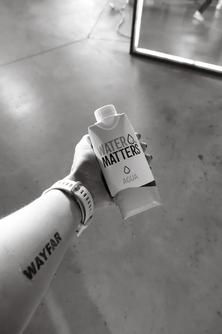 Una mano con reloj deportivo sostiene un envase de Water Matters de 330 ml en una competencia