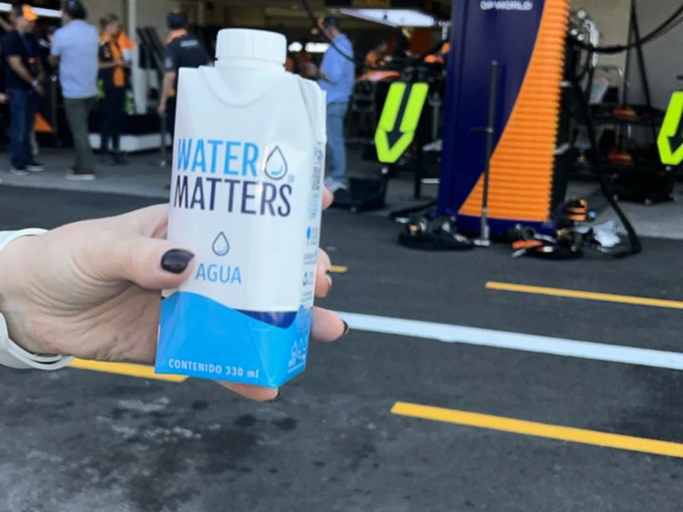 Un envase de Water Matters de 330 ml sostenido en el pit lane, frente a los boxes